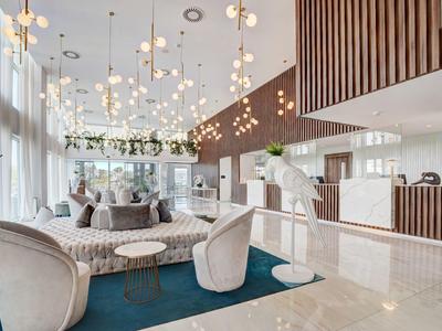 Moderner, heller Wohnbereich mit großen Fenstern, Hängelampen, gemütlichen Sesseln und blauem Teppich.