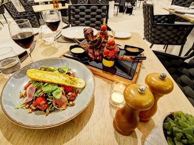 Ein Tisch mit Essen, darunter ein Sandwich, Rotwein und Holzgewürzmühlen auf hellem Holz.