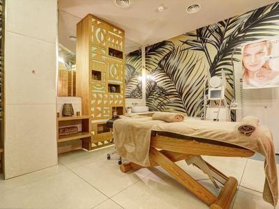 Schöner Behandlungsraum mit Massageliege, tropischer Tapete und warmem Licht in hellen Tönen.