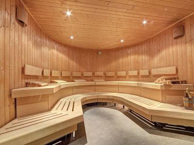 Sauna mit gebogenem Holz-Sitzbereich, Holzverkleidung und sanfter Deckenbeleuchtung.
