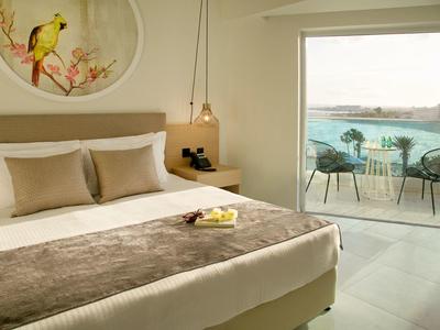 Gemütliches Schlafzimmer mit Doppelbett, hellen Tönen und Balkon mit Meerblick und Sitzbereich.