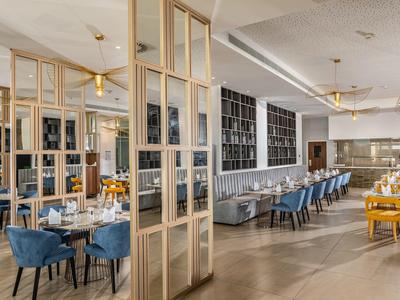 Großer, heller Gastraum mit blauen Sesseln, gedeckten Holztischen und modernem Dekor.