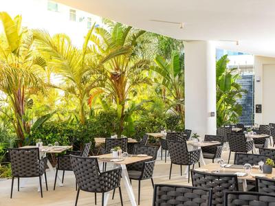 Moderne Außenterrasse mit schwarzen Stühlen, Tischen und üppigem grünem Palmenhintergrund.