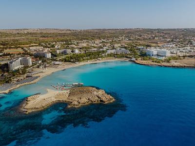 Vue aérienne d'une ville côtière avec une mer bleue, des plages de sable et des bâtiments le long du rivage.