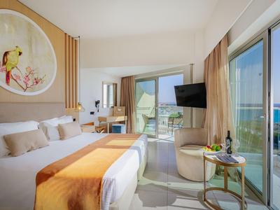 Chambre d'hôtel lumineuse avec lit double, balcon et vue sur la mer en plein jour.