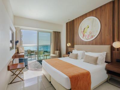 Chambre d'hôtel lumineuse avec lit double, mur en bois et vue sur la mer par de grandes fenêtres