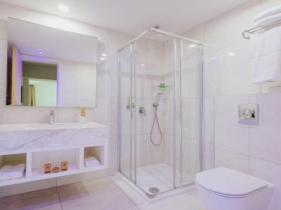 Salle de bains moderne et lumineuse avec douche, toilettes, lavabo et serviettes au mur.