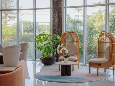Espace de détente moderne avec grandes fenêtres et plantes pour une ambiance d'hôtel détendue.