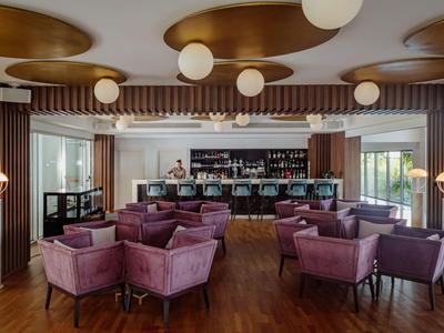 Bar d'hôtel élégante avec fauteuils violets, lampes modernes et sol en bois dans une ambiance chaleureuse.