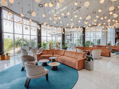 Hall d'hôtel moderne avec lampes suspendues rondes, canapés marron et grandes fenêtres donnant sur la verdure.