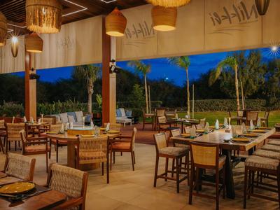 Espace de restaurant ouvert avec mobilier en bois et vue sur le jardin au crépuscule.