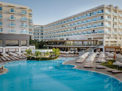 Hôtel moderne avec grande piscine et transats en extérieur sous un ciel dégagé.