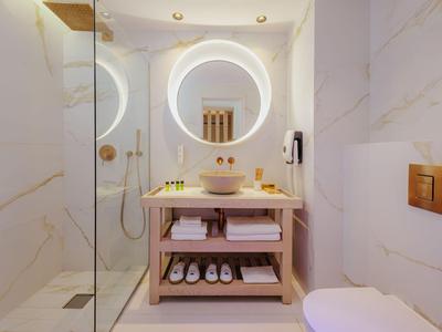 Salle de bain moderne avec miroir rond éclairé, meuble en bois et douche en verre.