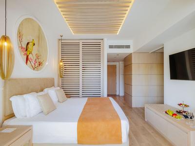 Chambre d'hôtel lumineuse avec lit double, couvre-lit orange et grande télévision murale.