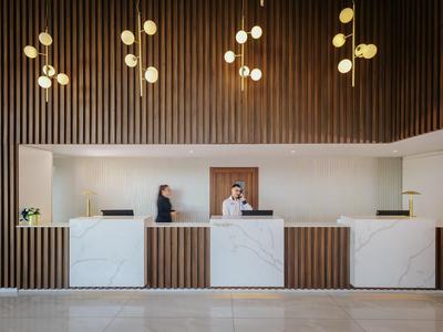 Hall d'hôtel moderne avec panneaux en bois, comptoir en marbre blanc et luminaires suspendus décoratifs.