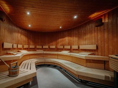 Salle de sauna avec bancs en bois courbés et éclairage doux pour une expérience de bien-être relaxante.