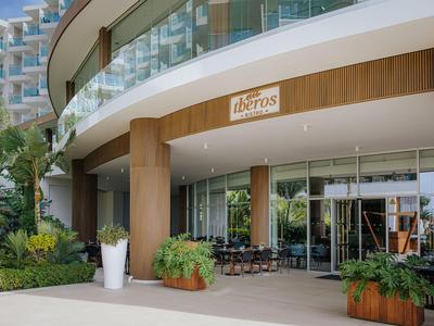 Entrée d'hôtel moderne avec façade en verre, espace de seating et plantes extérieures.