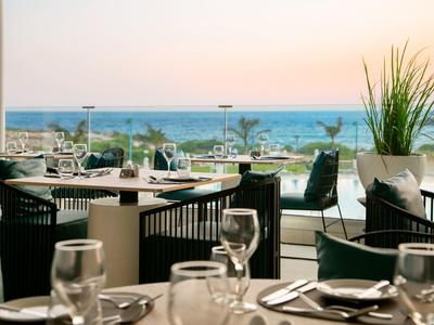 Restaurantterrasse mit gedeckten Tischen, Stühlen und Blick auf das Meer im Sonnenuntergang.