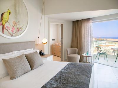 Helles Schlafzimmer mit großem Bett, gemütlichen Kissen, modernem Stuhl und Balkon mit Meerblick.