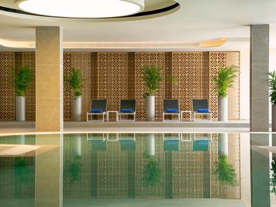 Espace piscine intérieure moderne avec sièges et plantes devant un mur en pierre.