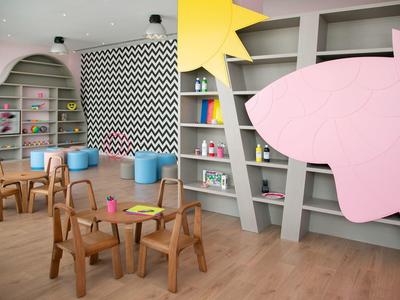 Kindergartenraum mit Holztischen, Stühlen, bunten Regalen und einem großen gelben Stern an der Wand.