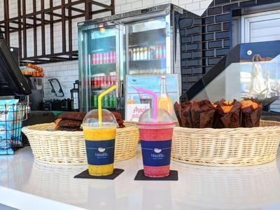 Deux boissons colorées avec couvercles et pailles devant un panier de muffins dans un café.