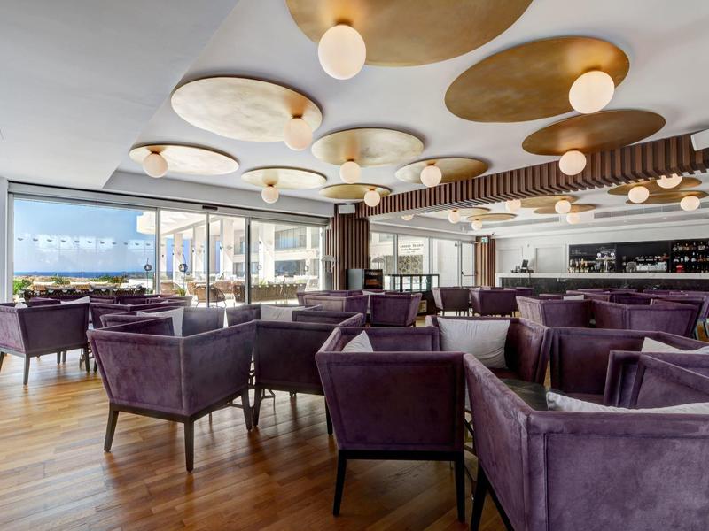 Moderner Gastraum mit lila Sesseln, Holzboden, großen Fenstern und dekorativer Decke mit runden Elementen.