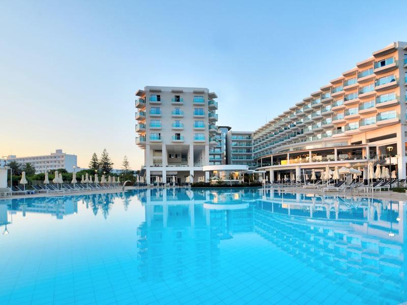 Großes Hotelgebäude mit einem blauen Swimmingpool im Vordergrund und klarem Himmel.