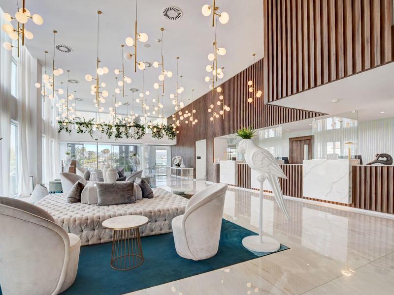 Moderner, heller Wohnbereich mit großen Fenstern, Hängelampen, gemütlichen Sesseln und blauem Teppich.