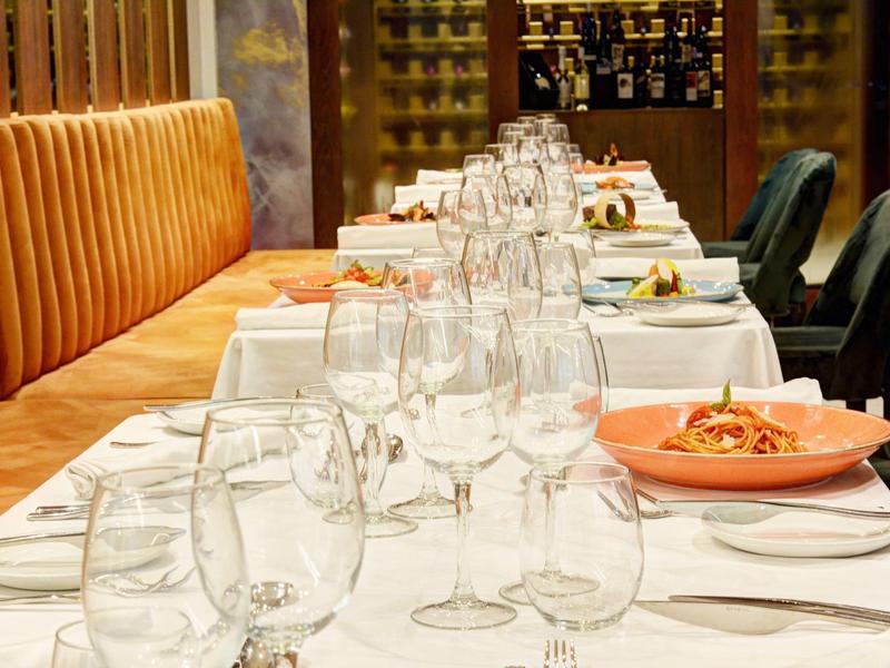 Eleganter, lang gedeckter Esstisch mit weißen Tischdecken, Gläsern und orangenen Tellern im Restaurant.