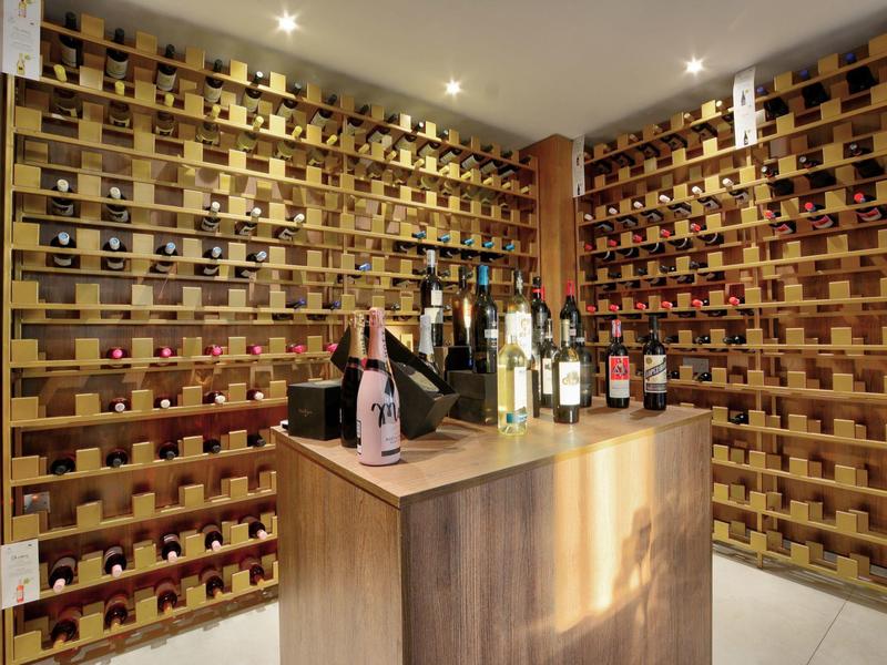 Weinkeller mit Holzwänden voller Weinflaschen und einem zentralen Holztresen mit weiteren Flaschen.