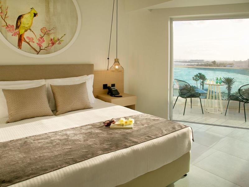 Gemütliches Schlafzimmer mit Doppelbett, hellen Tönen und Balkon mit Meerblick und Sitzbereich.