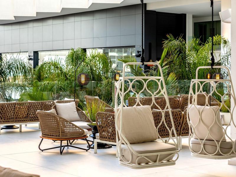 Moderner Außenbereich mit hellen Hängestühlen, Korbmöbeln und grünen Pflanzen auf heller Terrasse.