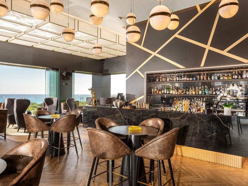 Modernes Café mit dunklem Barbereich, Lederstühlen, Holzboden und großen Fenstern mit Meerblick.