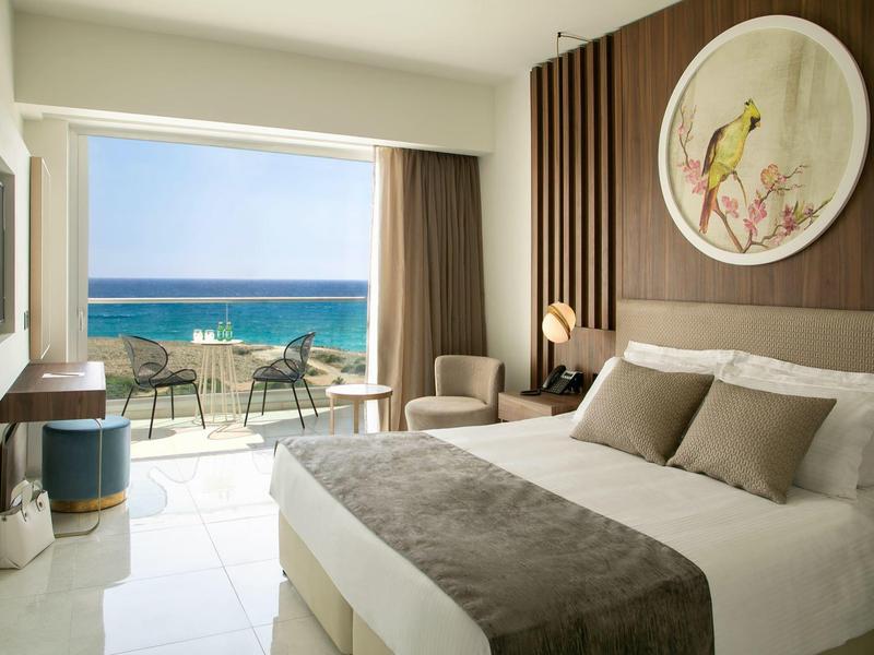 Modernes Hotelzimmer mit Doppelbett, Holzwandverkleidung und Balkon mit Meerblick und Gartenmöbeln.