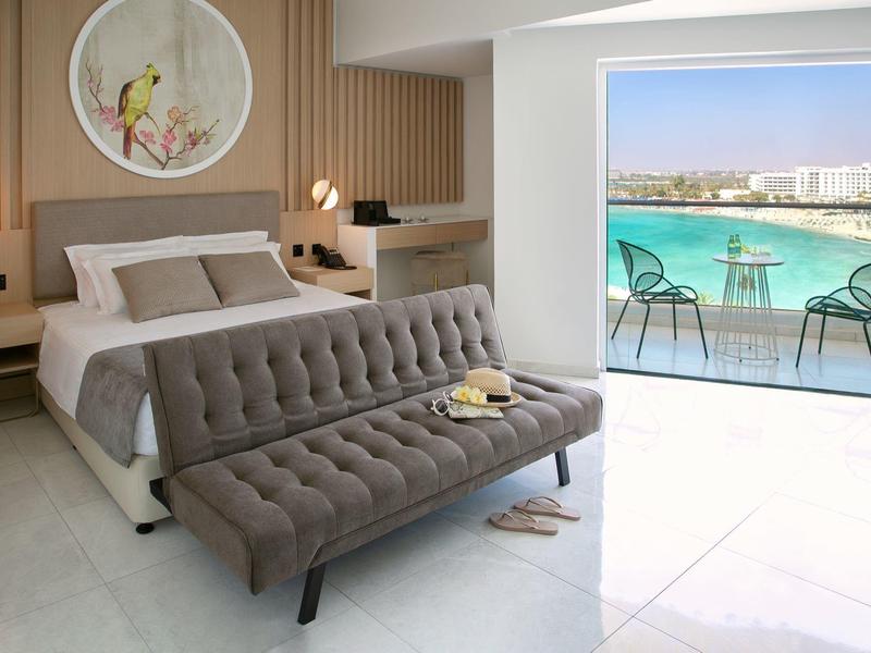 Modernes Schlafzimmer mit grauem Bett und Sofa, Balkon mit Blick auf blauen Pool und Stadt.