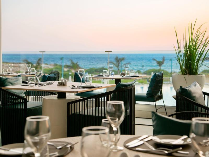 Restaurantterrasse mit gedeckten Tischen, Stühlen und Blick auf das Meer im Sonnenuntergang.