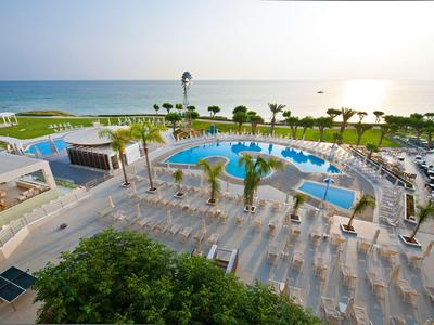 Hotelový bazén s lehátky, palmami a výhledem na moře při západu slunce.