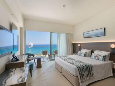 Modernes Hotelzimmer mit großem Bett, Meerblick durch Fenster und hellem Interieur.