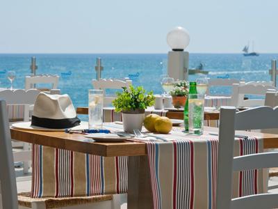 Tafel met hoed, drankjes en decoratie met uitzicht op de zee en strandstoelen.