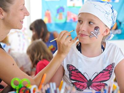Kind met vlinder T-shirt krijgt gezicht beschilderd in vrolijke omgeving.