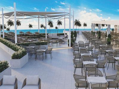 Otevřená restaurace s mnoha stoly a židlemi u moře pod modrou oblohou.