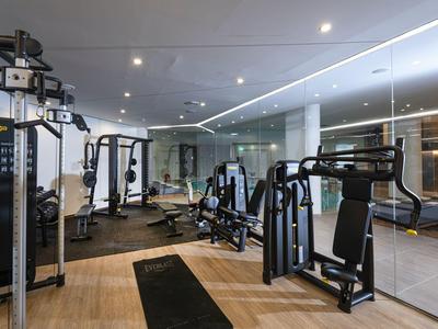 Moderní fitness s různými tréninkovými stroji a velkým zrcadlem na stěně.