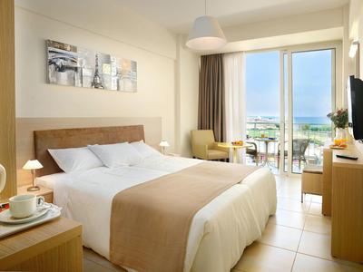 Lichte hotelkamer met tweepersoonsbed, balkon en zeezicht.