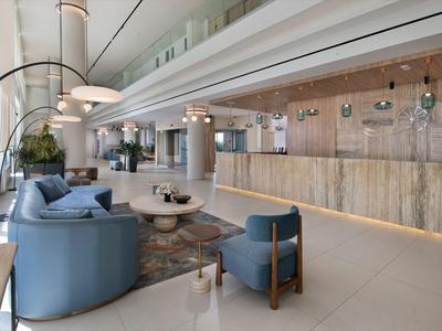 Modernes Hotelinterieur mit blauen Sitzmöbeln, Teppich und beleuchtetem Holzreszeptionsbereich.