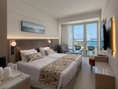 Helles Hotelzimmer mit Doppelbett, Balkon und Blick auf das Wasser.