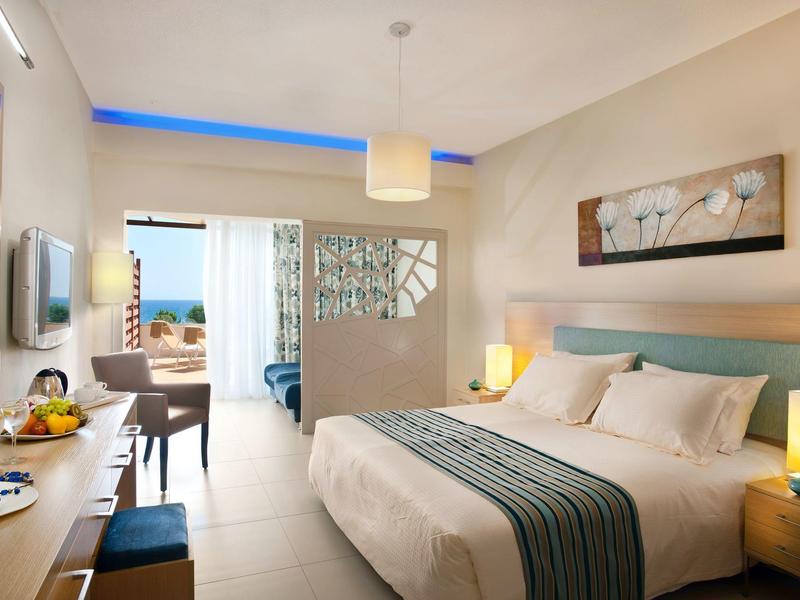 Modern hotelkamer met groot bed, bureau en uitzicht op zee.