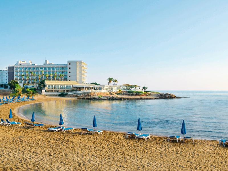 Zandstrand met blauwe parasols en hotelgebouw aan zee bij heldere lucht.