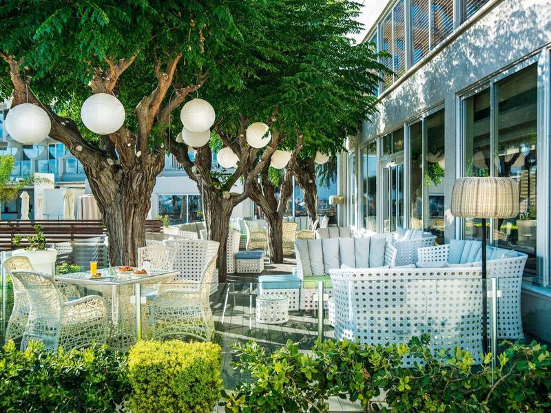 Gezellige buitenzitplekken met wit meubilair en bomen naast een modern gebouw.