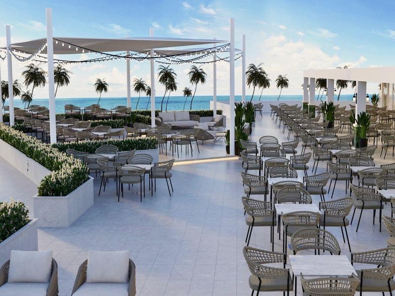 Groot dakterras met tafels, stoelen, planten en zeezicht onder een heldere hemel.